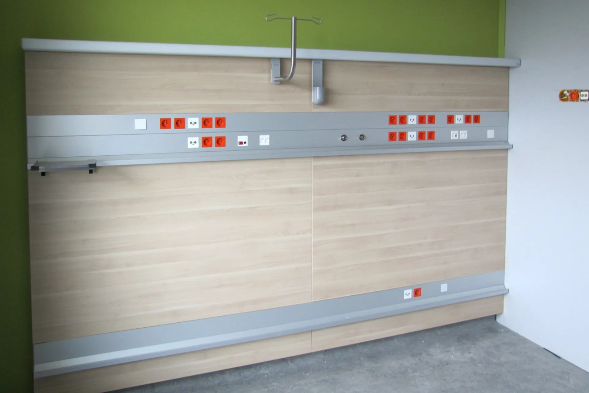 Wall with several sockets and connections in a room with a green-painted wall and a grey floor