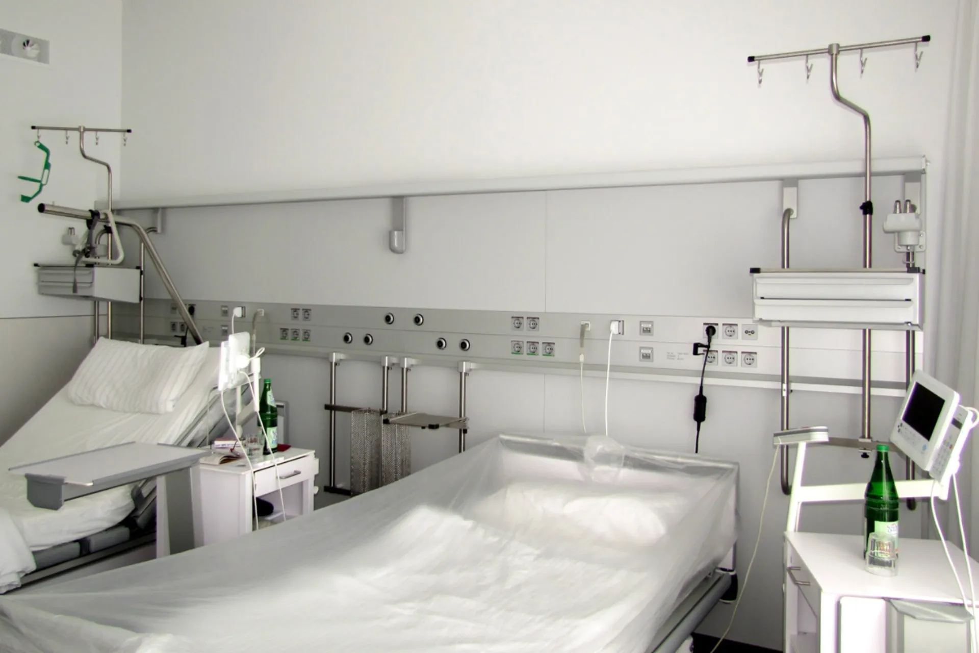 A twin hospital room with a horizontal equipment rail on the rear wall.