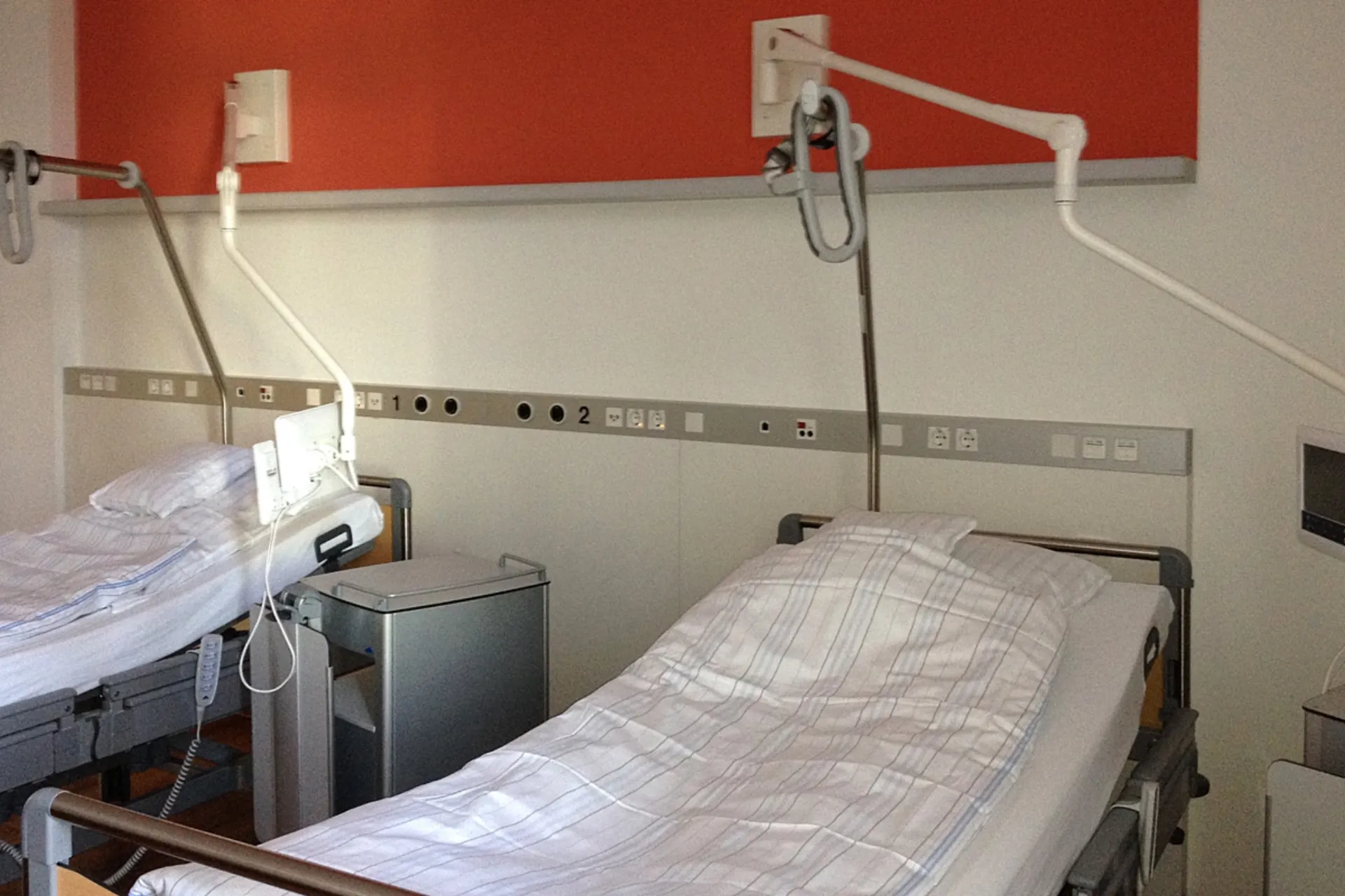 Two hospital beds with white bed linen and adjustable reading lamps on the wall in a patient room