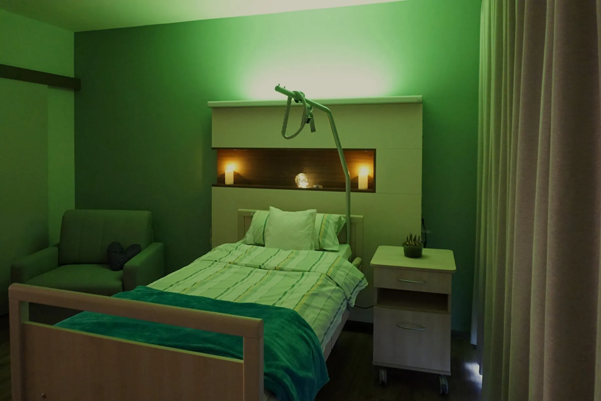 Ein Einzelbett mit Kopfteilbeleuchtung und einem Nachttisch in einem in grünes Licht getauchten Zimmer