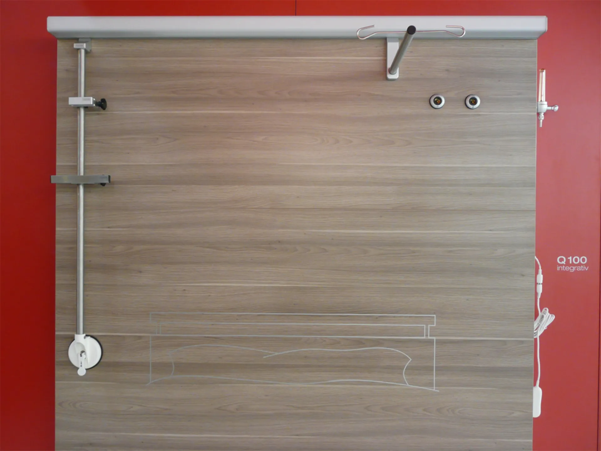 Wooden panel with metal bars and rollers on the left and top sides in front of a red wall with the white lettering 'Q100 integrativ'