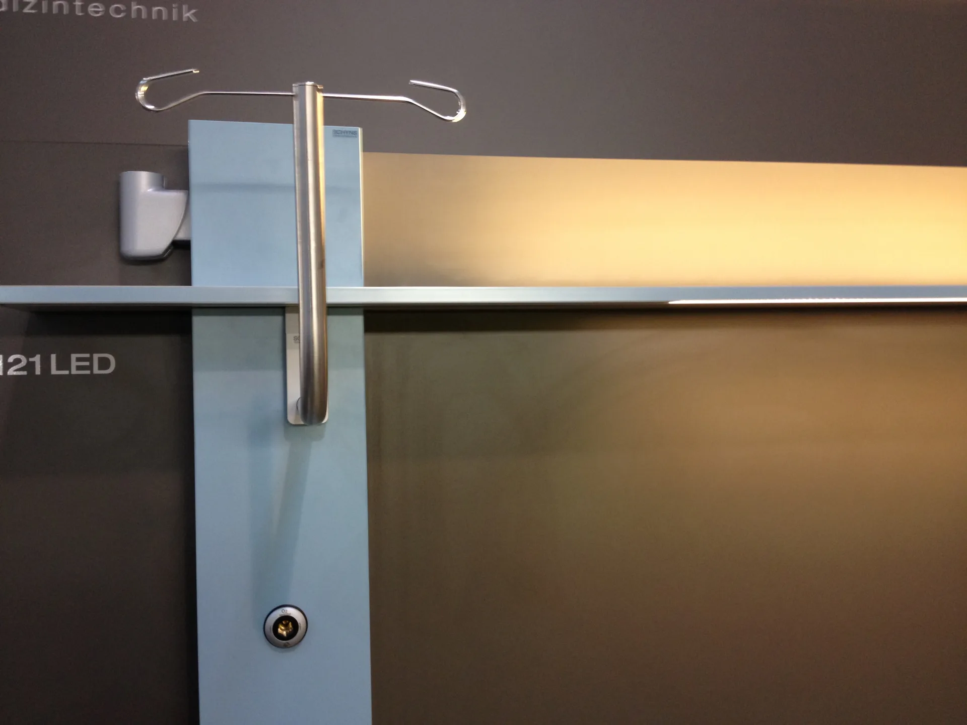 Detail shot of a pure supply unit with a light-blue front, a vertical chrome handle, an infusion holder and a medical gas connection against a dark background