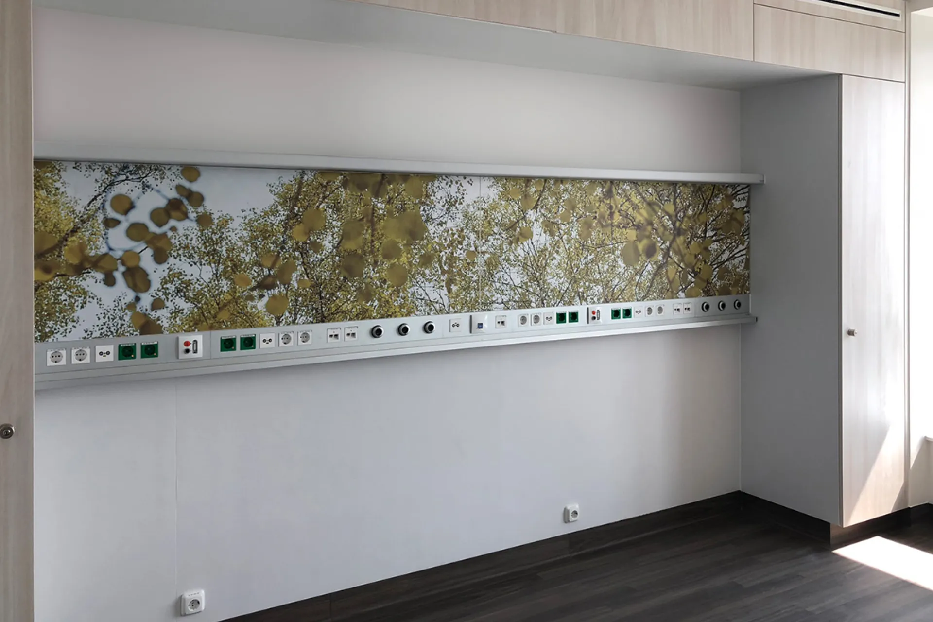 Wall-mounted supply unit with a socket strip and a digitally printed motif of branches against a blue sky