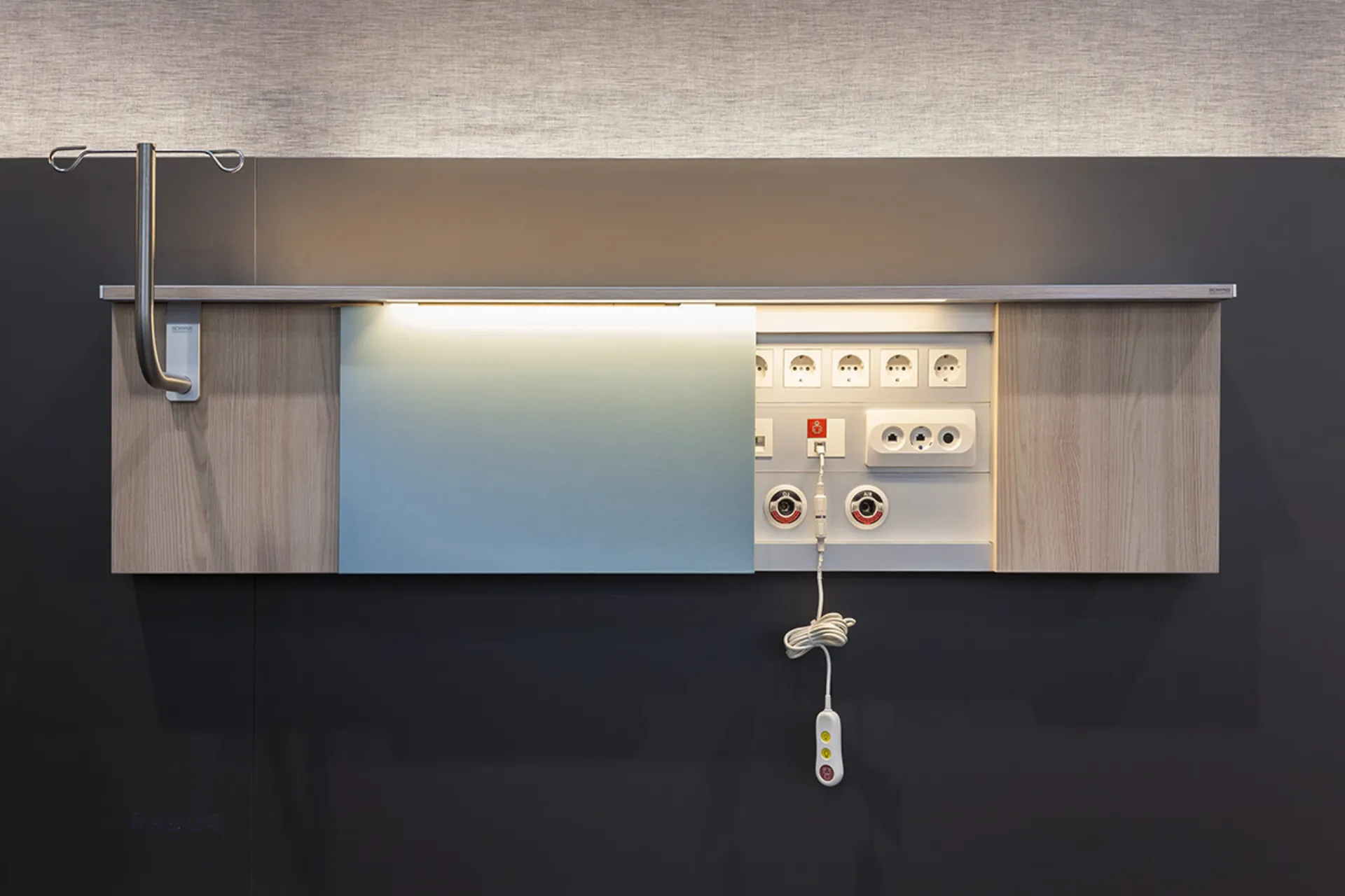 Wall-mounted medical supply unit with wood cladding, several sockets, medical gas connections, an infusion stand and a hanging control unit