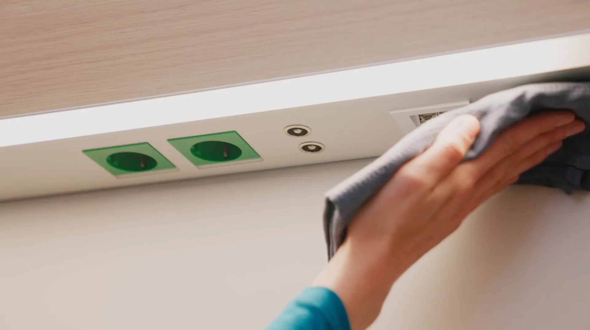 Close-up of a hand with a cloth wiping across the flush-mounted rail with socket and connections